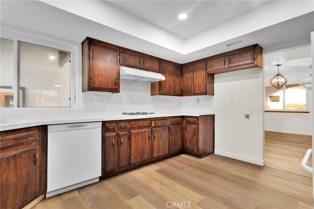 kitchen with gas stovetop, a tray ceiling, white dishwasher, light hardwood / wood-style floors, and backsplash