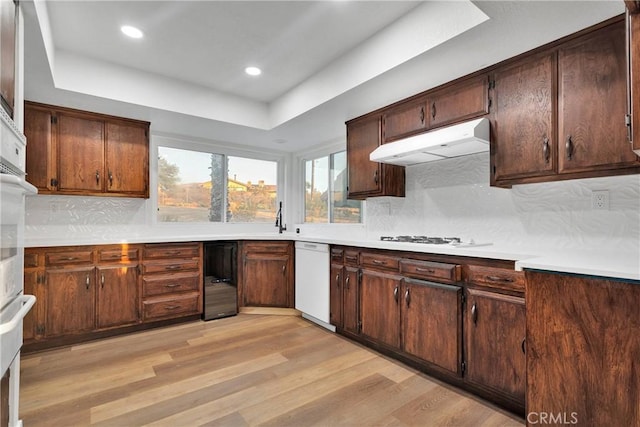 kitchen featuring white appliances, light hardwood / wood-style floors, backsplash, and a tray ceiling