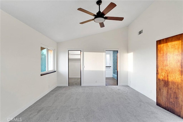 unfurnished bedroom featuring high vaulted ceiling, carpet flooring, connected bathroom, a walk in closet, and a closet