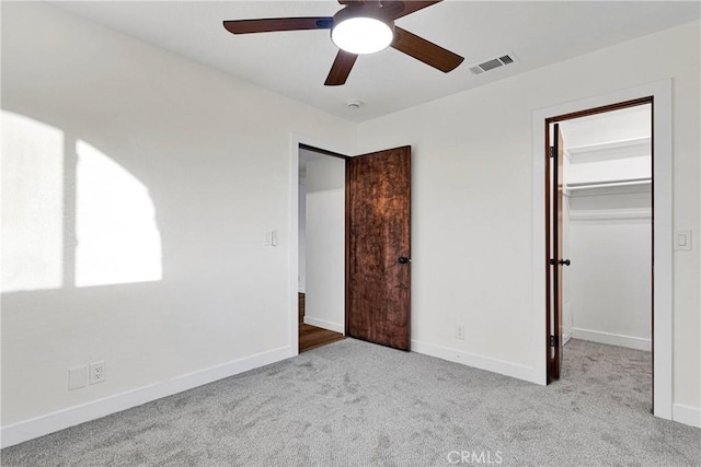 unfurnished bedroom featuring light carpet, a spacious closet, a closet, and ceiling fan