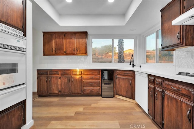 kitchen featuring white appliances, a raised ceiling, sink, light hardwood / wood-style flooring, and tasteful backsplash