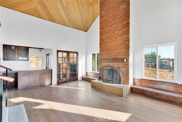 unfurnished living room with high vaulted ceiling, hardwood / wood-style flooring, a brick fireplace, wooden ceiling, and french doors