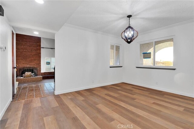 unfurnished room with crown molding, a fireplace, a chandelier, and light hardwood / wood-style flooring