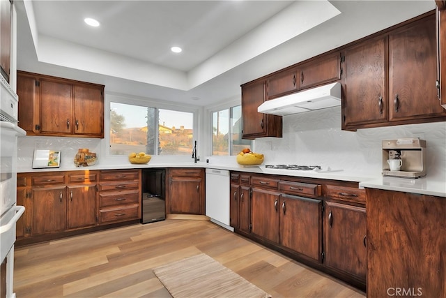 kitchen with white appliances, decorative backsplash, a tray ceiling, sink, and light hardwood / wood-style flooring