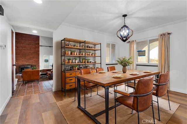 dining room featuring a brick fireplace, light wood-type flooring, a notable chandelier, and crown molding