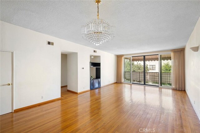 unfurnished living room with light wood-type flooring, a chandelier, and a textured ceiling