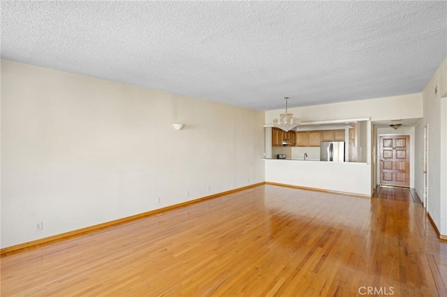 unfurnished living room with a textured ceiling, a chandelier, and light hardwood / wood-style flooring