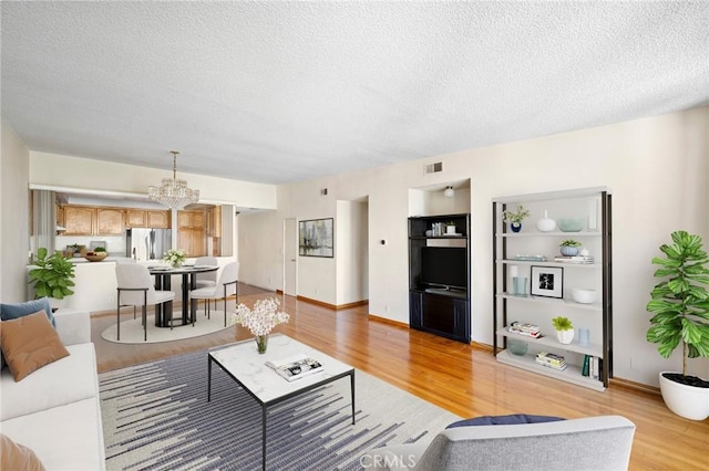 living room with built in shelves, a textured ceiling, a chandelier, and light hardwood / wood-style flooring