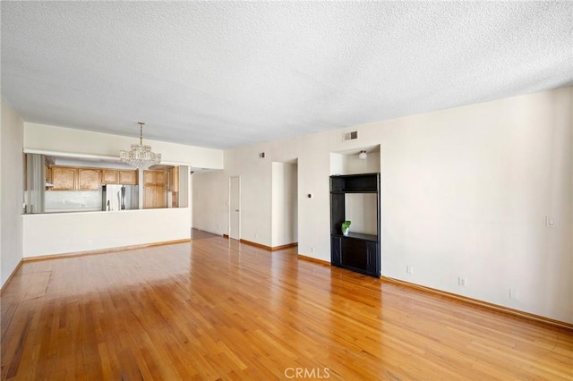 unfurnished room with a textured ceiling, light hardwood / wood-style flooring, and a notable chandelier