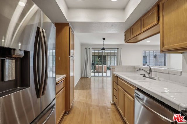 kitchen featuring light hardwood / wood-style floors, stainless steel appliances, tile counters, pendant lighting, and sink