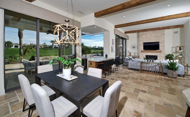 dining area featuring a notable chandelier, a stone fireplace, and beamed ceiling