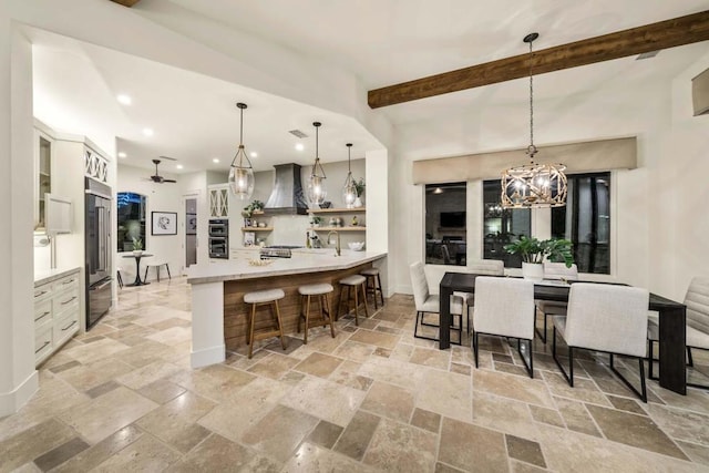 kitchen featuring pendant lighting, wall chimney range hood, a breakfast bar, and beamed ceiling