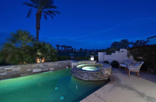 pool at night featuring an in ground hot tub