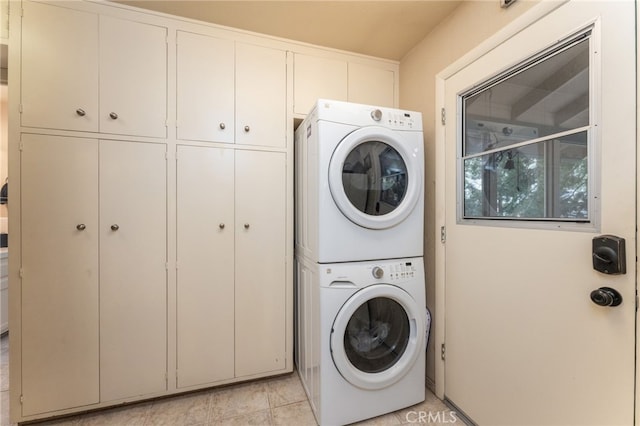 clothes washing area featuring stacked washer and dryer and cabinets