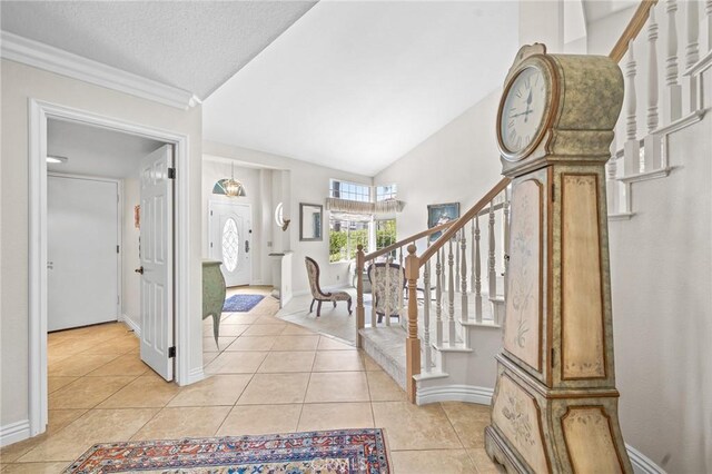 foyer entrance with a textured ceiling, light tile patterned floors, lofted ceiling, and crown molding