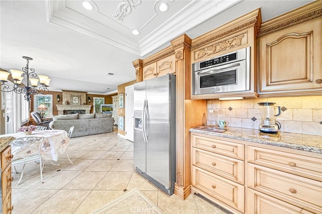 kitchen with light tile patterned floors, appliances with stainless steel finishes, a notable chandelier, a large fireplace, and crown molding