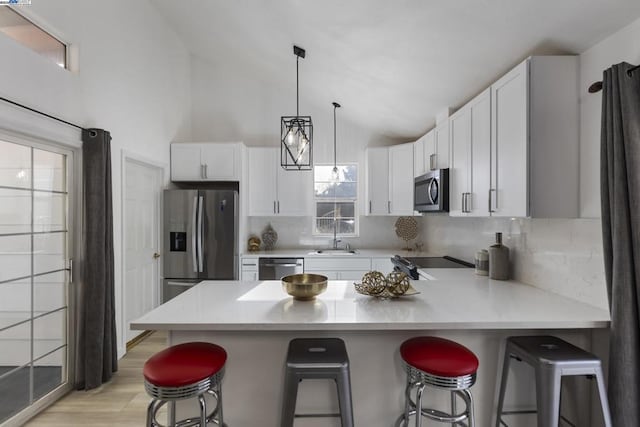 kitchen featuring a kitchen bar, appliances with stainless steel finishes, white cabinetry, and pendant lighting