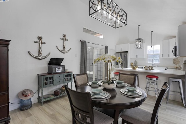 dining room featuring a towering ceiling, sink, light hardwood / wood-style flooring, and a chandelier