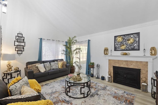 living room featuring light hardwood / wood-style floors, ornamental molding, lofted ceiling, and a tiled fireplace