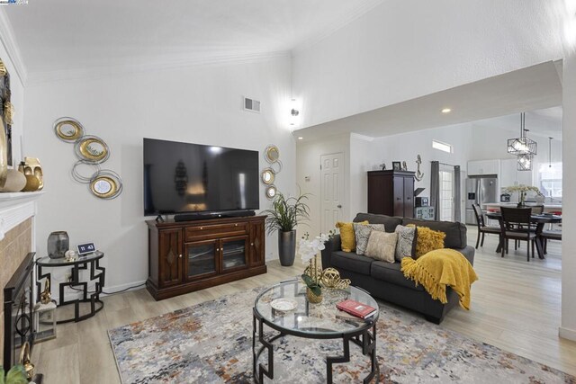 living room with an inviting chandelier, light hardwood / wood-style floors, ornamental molding, high vaulted ceiling, and a tiled fireplace