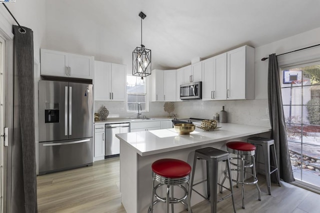 kitchen featuring a breakfast bar, sink, white cabinetry, hanging light fixtures, and appliances with stainless steel finishes