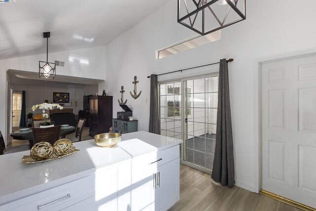 kitchen with lofted ceiling, white cabinets, hanging light fixtures, light stone countertops, and light hardwood / wood-style flooring