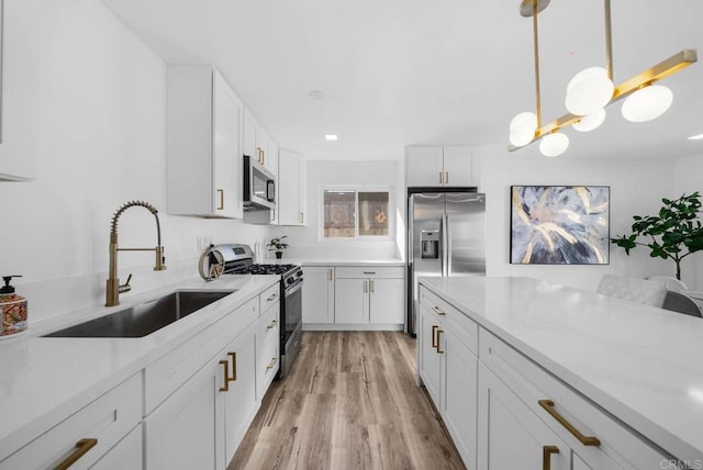 kitchen with white cabinetry, appliances with stainless steel finishes, decorative light fixtures, light wood-type flooring, and sink