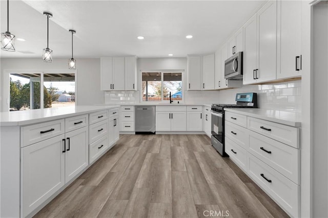 kitchen with tasteful backsplash, decorative light fixtures, white cabinetry, light wood-type flooring, and stainless steel appliances