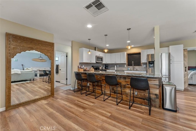 kitchen featuring light stone countertops, white cabinets, appliances with stainless steel finishes, backsplash, and light hardwood / wood-style flooring