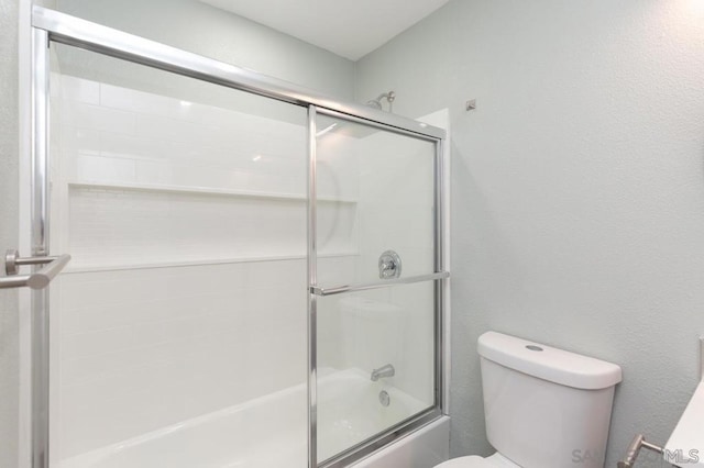 bathroom featuring combined bath / shower with glass door and toilet