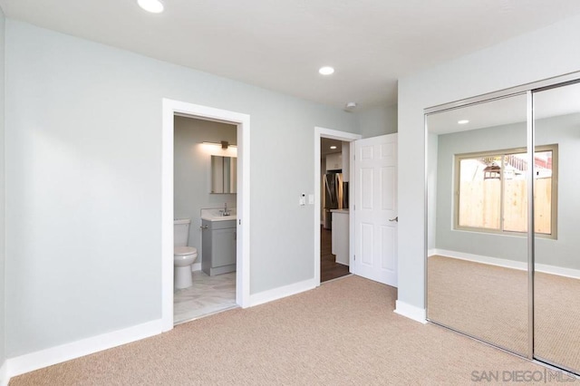 unfurnished bedroom featuring sink, stainless steel fridge, a closet, carpet flooring, and ensuite bathroom