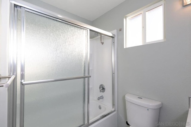 bathroom with toilet and shower / bath combination with glass door