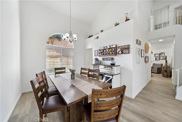 dining room with light hardwood / wood-style floors, high vaulted ceiling, and a notable chandelier