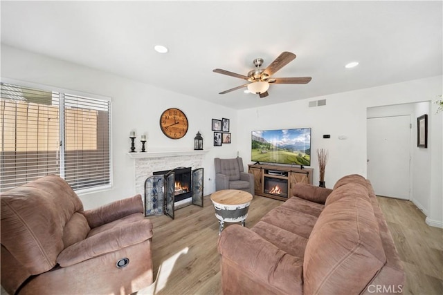 living room with light hardwood / wood-style flooring, a stone fireplace, and ceiling fan