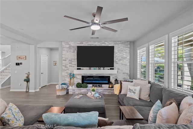 living room with ceiling fan, a stone fireplace, and light hardwood / wood-style flooring