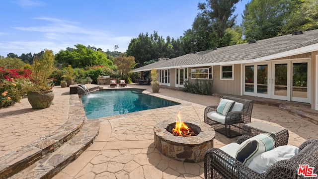 view of pool featuring pool water feature, a patio area, an outdoor living space with a fire pit, and french doors