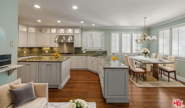 kitchen with an inviting chandelier, dark hardwood / wood-style floors, decorative light fixtures, a kitchen island, and wall chimney exhaust hood