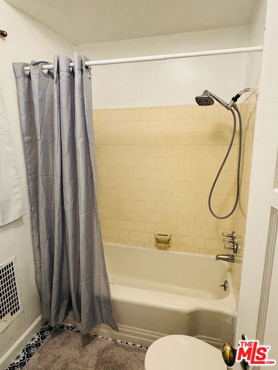 bathroom featuring toilet and shower / bathtub combination with curtain