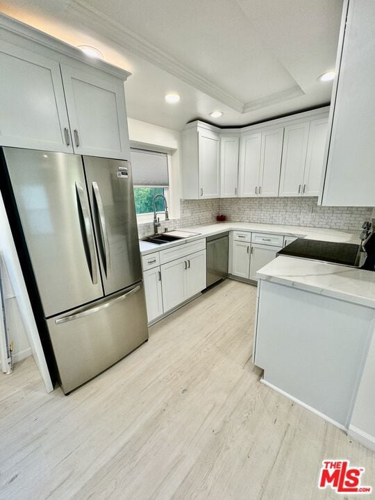 kitchen featuring stainless steel appliances, light wood-type flooring, white cabinets, light stone counters, and sink