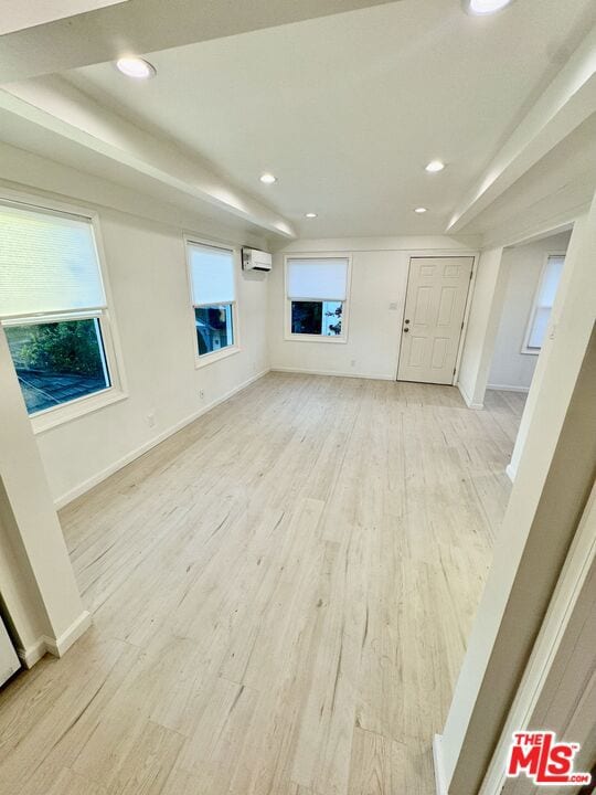 unfurnished living room featuring light wood-type flooring and a wall mounted air conditioner