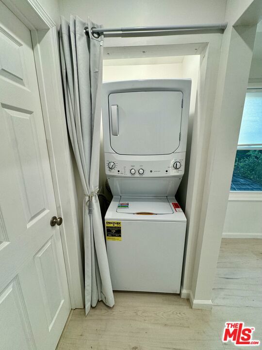 laundry room featuring stacked washing maching and dryer and light wood-type flooring