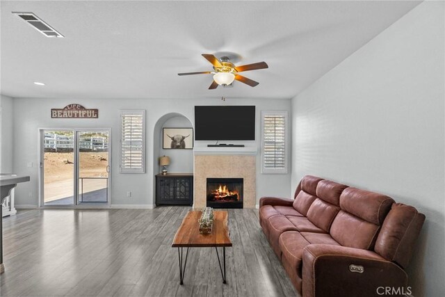 living room with ceiling fan, a tiled fireplace, and wood-type flooring