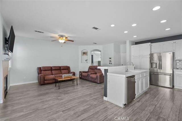 kitchen with appliances with stainless steel finishes, a kitchen island with sink, light wood-type flooring, white cabinets, and sink