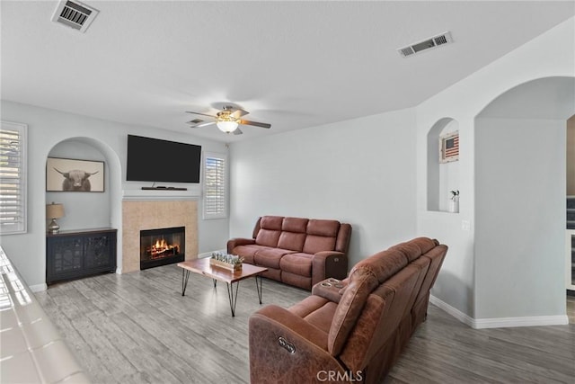 living room featuring ceiling fan, a tiled fireplace, a wealth of natural light, and hardwood / wood-style floors