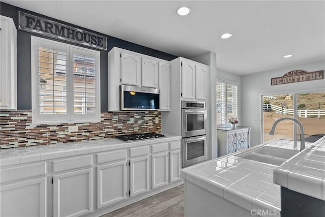 kitchen with appliances with stainless steel finishes, tile counters, white cabinets, and sink