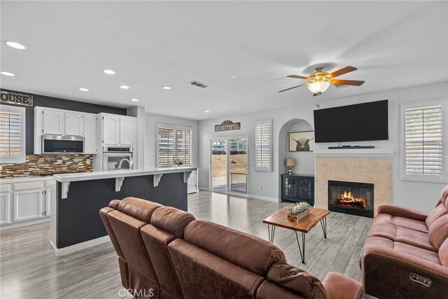 living room featuring ceiling fan, light hardwood / wood-style floors, a wealth of natural light, and a fireplace