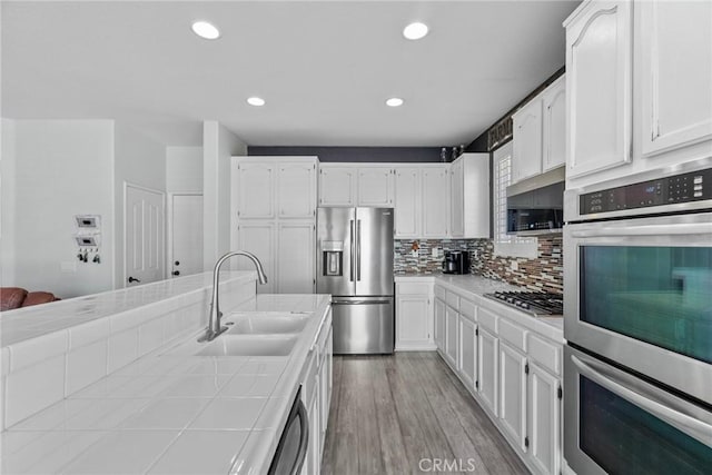 kitchen featuring tile counters, sink, white cabinetry, and stainless steel appliances