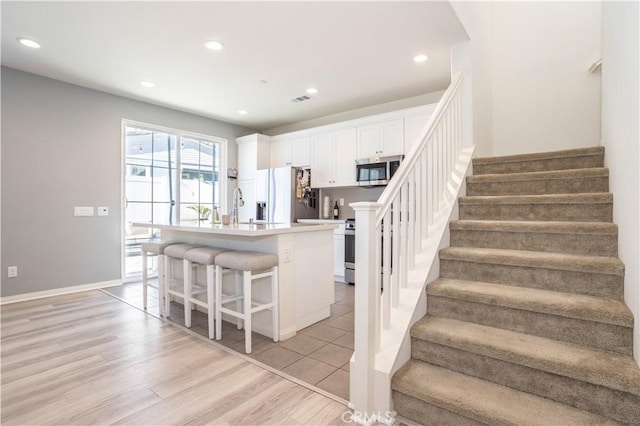 kitchen featuring a center island with sink, sink, a kitchen breakfast bar, stainless steel appliances, and white cabinets