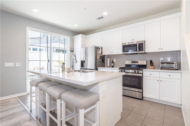 kitchen with white cabinets, a kitchen island with sink, appliances with stainless steel finishes, and a kitchen bar