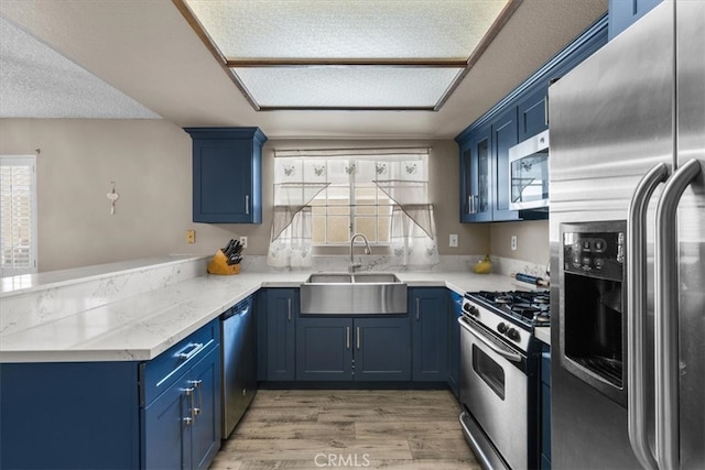 kitchen with appliances with stainless steel finishes, blue cabinets, wood-type flooring, a textured ceiling, and sink